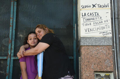 Dos personas se abrazan al lado de una pared con escrituras a favor de Milei el día de su asunción presidencial 2023